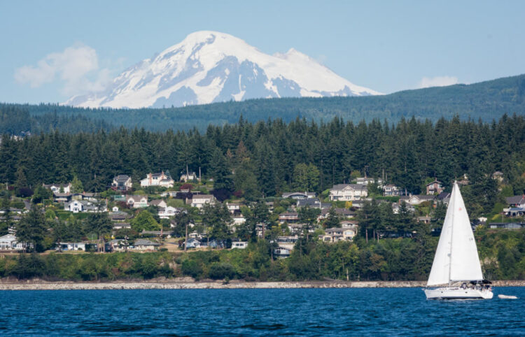 A photo of Mount Baker with a sailboat and houses in the Bellingham town area on the water, a beautiful coastal city in Washington.