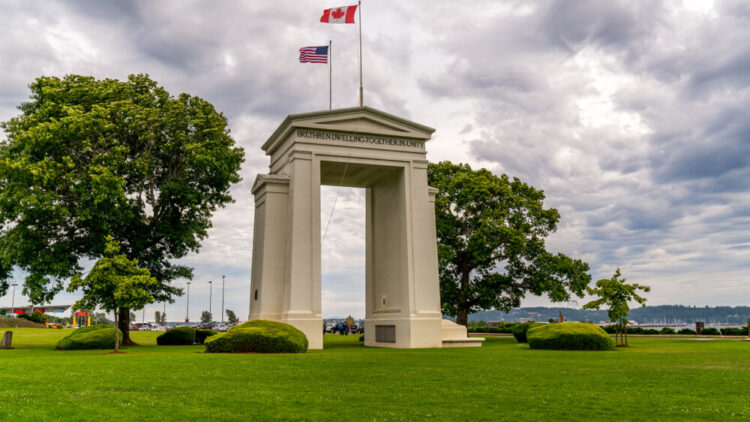 US Peace Arch border crossing. Canadian and US flags are waving in the wind on a beautiful cloudy sky.