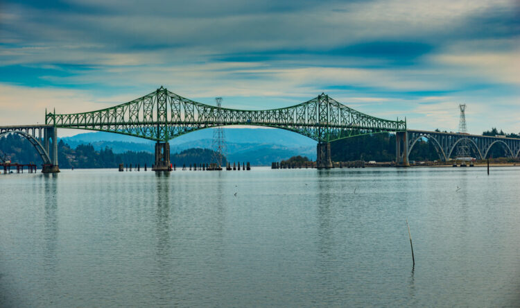 McCullough Memorial Bridge Bridge spans Coos Bay along U.S. Route 101 aka the pacific coast highway, mountains in the background and calm water below with streaky clouds