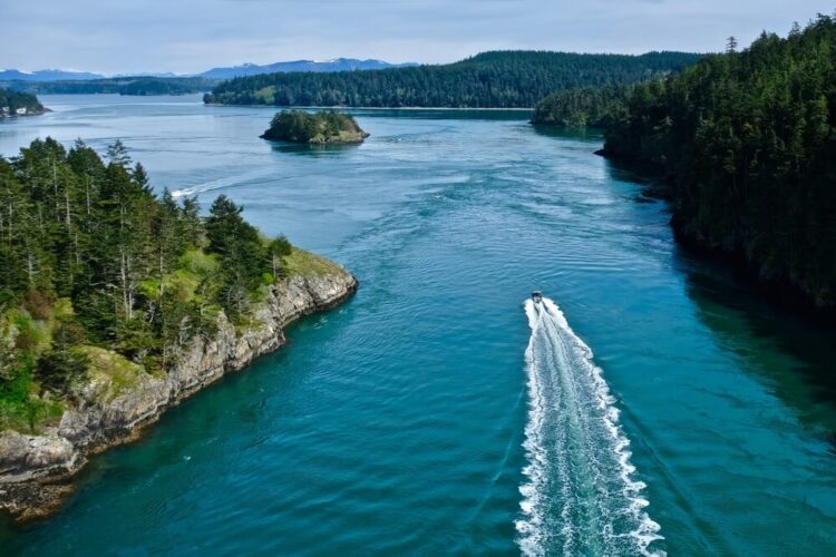 Boat in the ocean leaving a wake behind it, among islands with views of Deception Pass State Park in the Puget Sound.