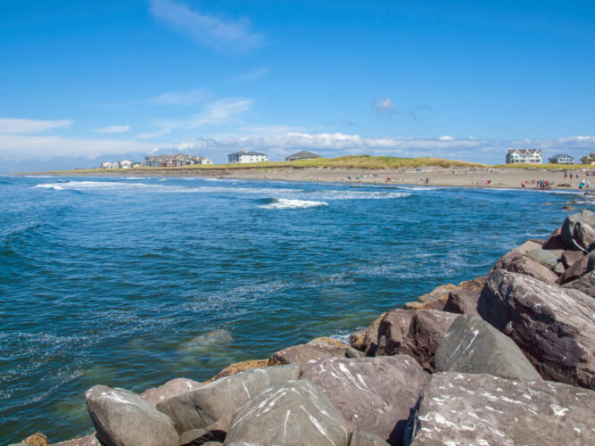 Rocks next to the Pacific Ocean with a view of a beach and coastal town in Washington in the distance on a sunny day in the Pacific Northwest