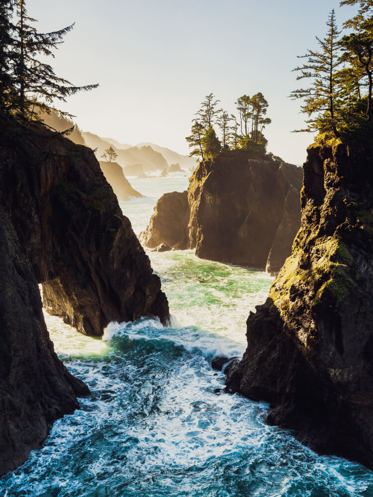 vertical image showing the sea stacks of the oregon coast at sunrise with warm light bathing the rock formations