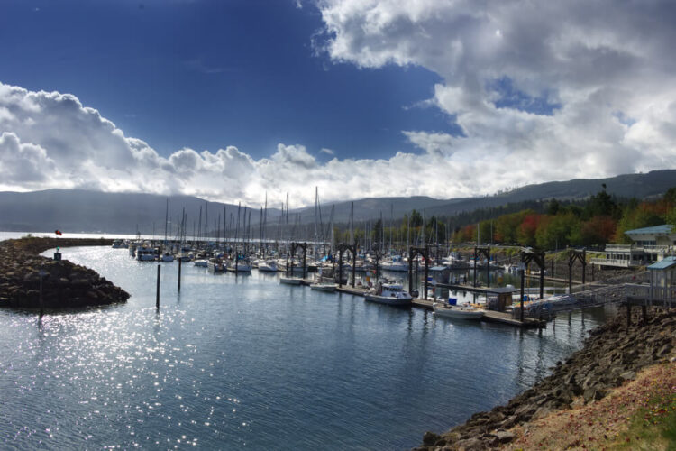 Boats in the marina of Sequim in the fall with some fall foliage in the trees in the distant background and a partly cloudy sky.