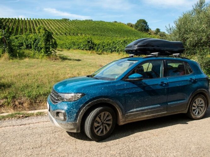 blue car with rack on top splattered with mud next to vineyards in oregon