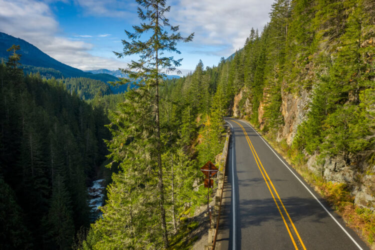 The scenic road of the Mt Baker Highway against pine trees and a river on one edge of the drive