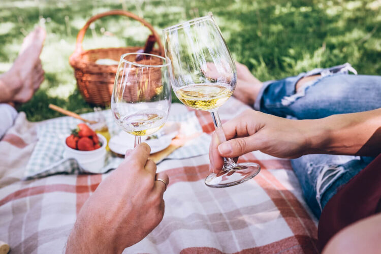 Hands cheersing with white wine while enjoying a picnic