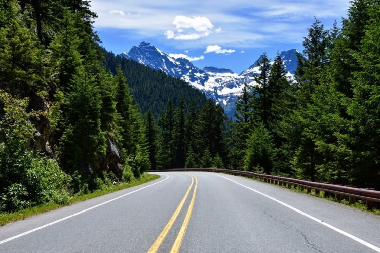 Hitting the open road on a two lane highway while driving in Washington state with snow-capped mountains in the distance.