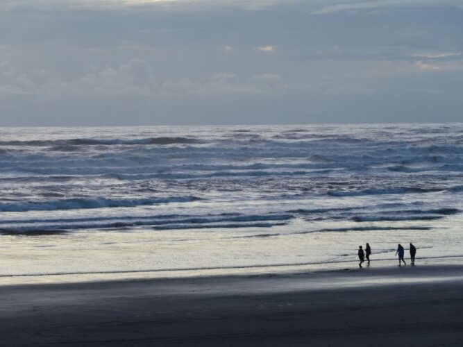 four people standing on the beach in the afternoon light